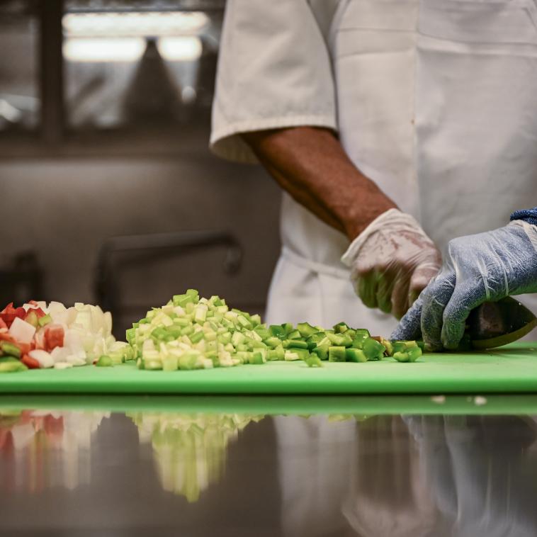 the hands of a chef in a professional kitchen are shown chopping a variety of vegetables on a cutting board