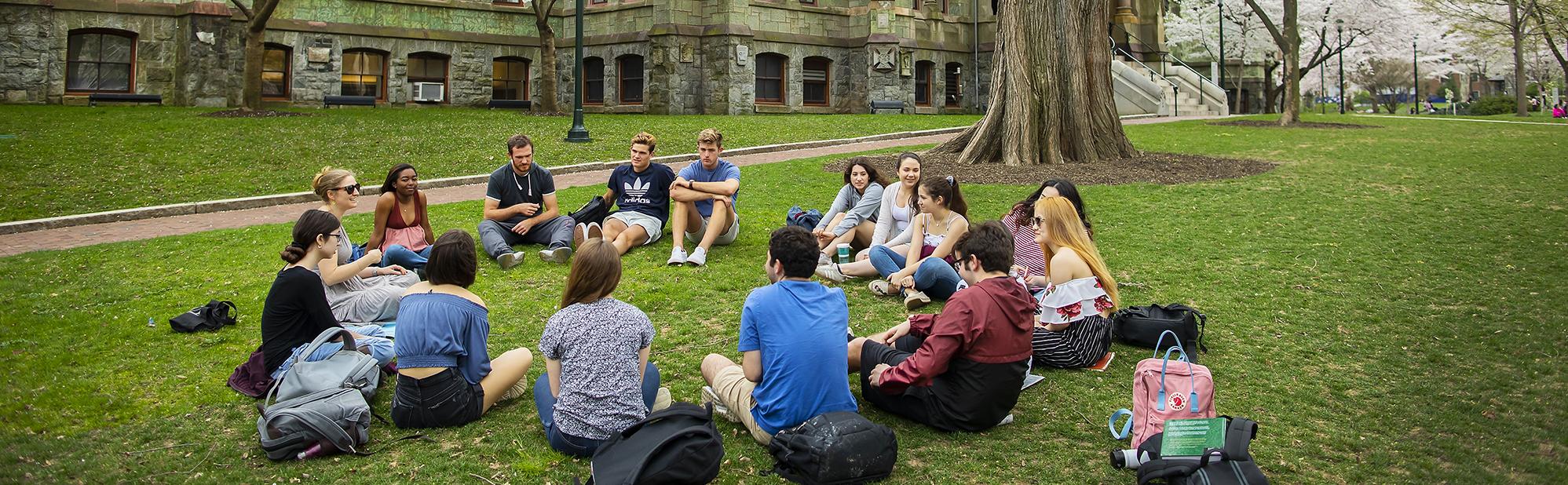 Students gathered in a circle on the lawn in spring under a flowering tree on Penn campus