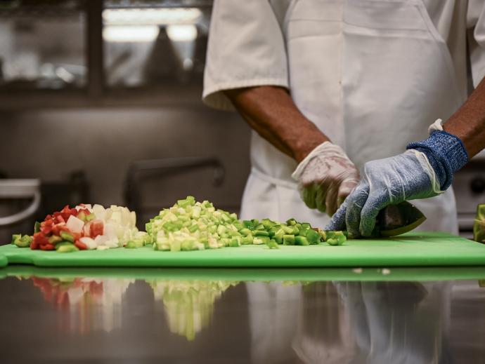 the hands of a chef in a professional kitchen are shown chopping a variety of vegetables on a cutting board