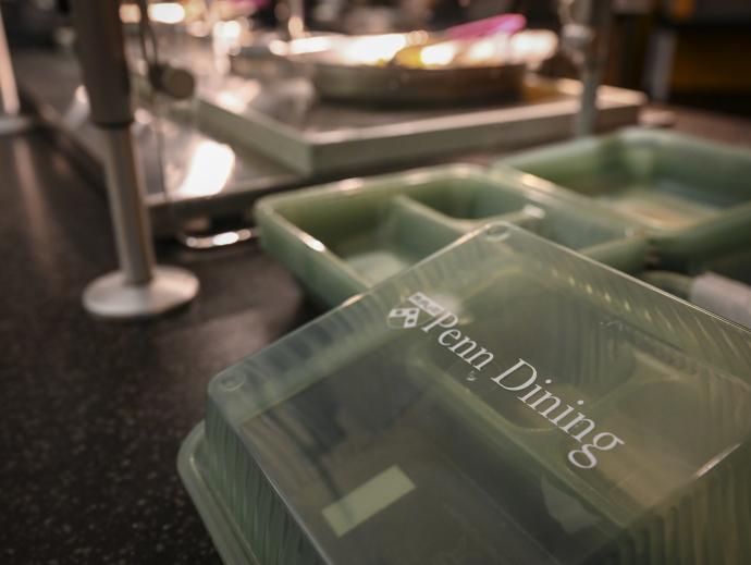 Take-out containers are shown near the buffet of a dining cafeteria. The containers are labelled "Penn Dining".
