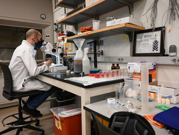 man in white coat at lab desk at microscope