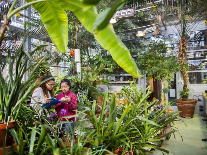 two female students taking notes in greenhouse