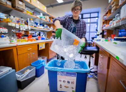 woman in a lab tipping items into larger container